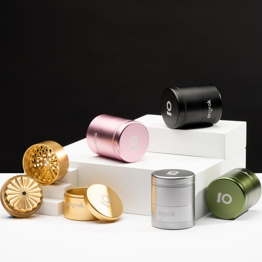 ONGROK aluminum grinders in five colors on white risers, one gold grinder opened to show its flower-petal toothless teeth