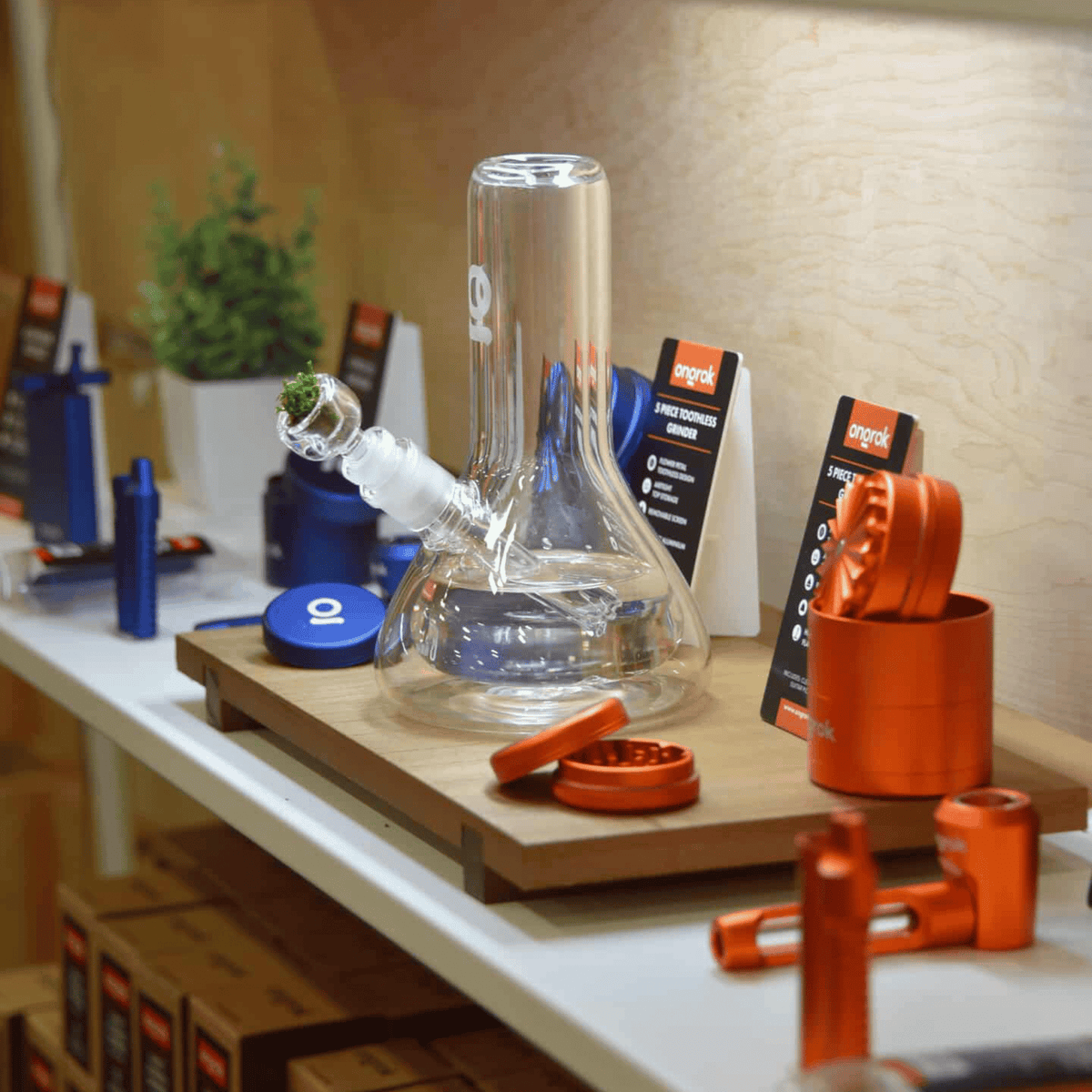 ONGROK retail shelf display with orange and blue aluminum grinders, storage jars, pipes and a glass water pipe
