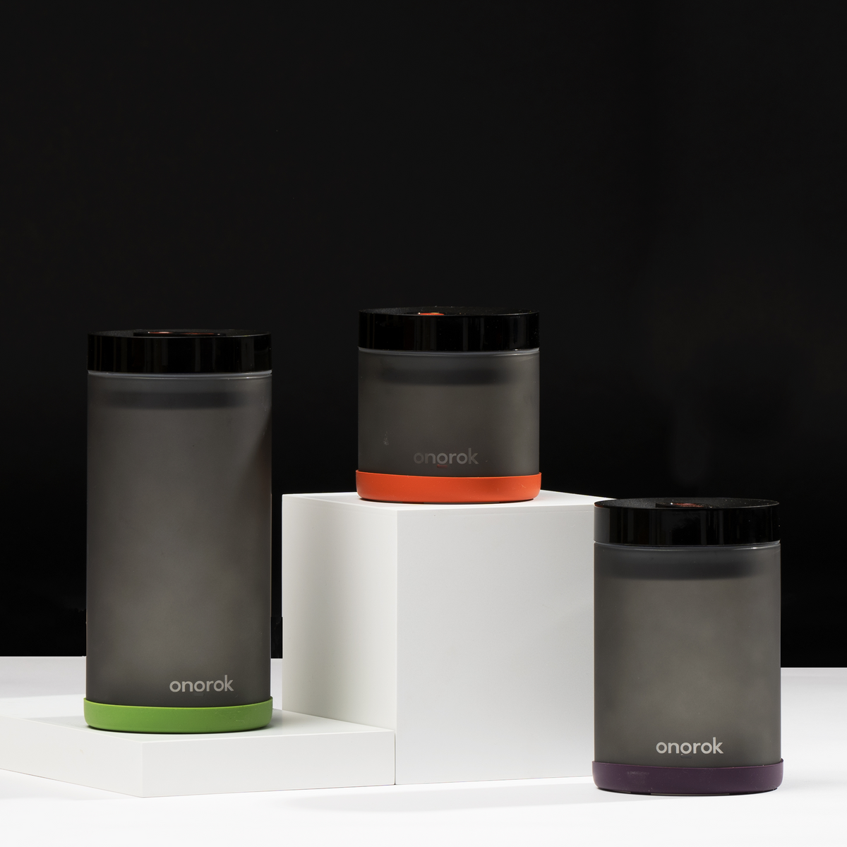 Three ONGROK frosted glass vacuum-seal storage jars with green, orange and purple bases on white risers